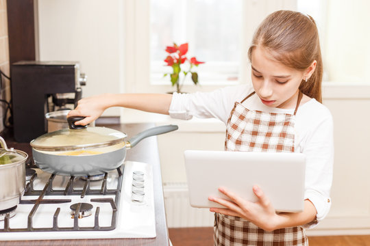 Small Teenage Girl Cooking On Cooker With Laptop