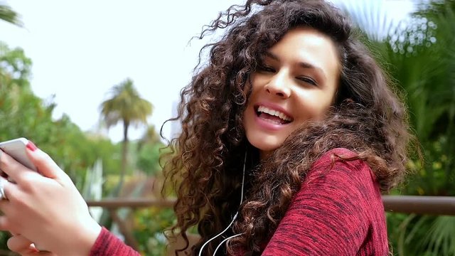 Young woman with beautiful curly hair listening to music in the park, slow motion