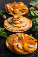 Tart with apricot and apple. Traditional french pie with fruits on dark marble background. Decorated almonds and mint leafs. Delicious dessert with copy space closeup.