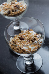 Granola with yoghurt, nuts and fruits in glass bowl on dark background. Delicious, healthy sweet dessert for breakfast. Cereal, muesli.  Copy space, closeup.