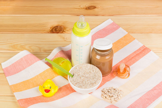 Bottle of milk, oatmeal, mashed potatoes,  nipple on  light wood.