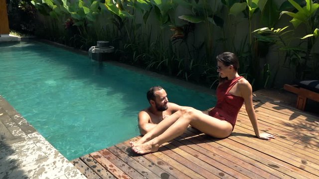 Young happy couple talking and relaxing by swimming pool, super slow motion
