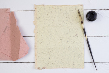 Top view of yellow paper, quill pen and ink on white deck table