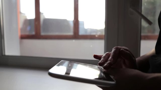 Woman near a window in his apartment using a tablet