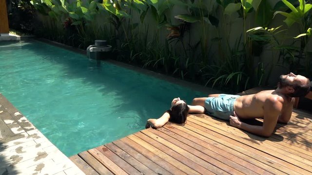 Young happy couple sunbathing by swimming pool, super slow motion
