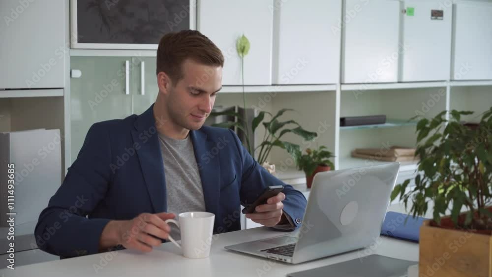 Aufkleber man smiling and texting sms on the mobile phone. on the table computer and cups.on the background sh