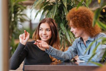 Two happy women talking in cafe and pointing away