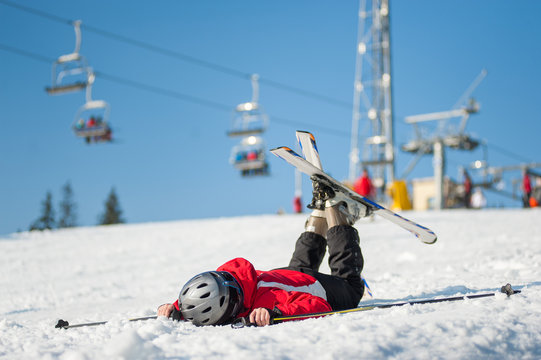 Skier lying face in the snow at mountain top in sunny day with ski lifts and blue sky in background