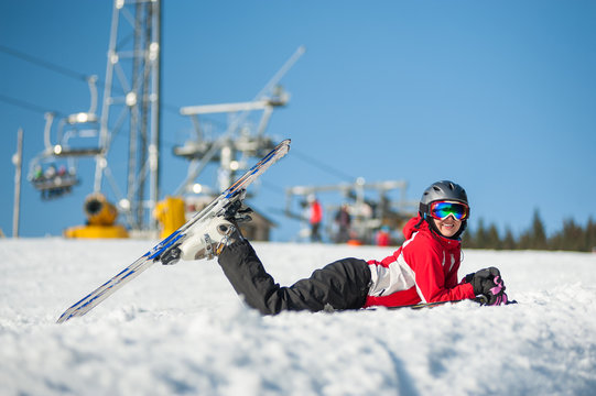 Portrait of female skier lying with skis on snowy at mountain top in sunny day with ski lifts and blue sky in background. Bukovel, Ukraine. Carpathian mountains