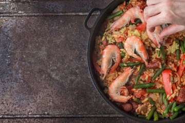 Adding prawns on the pan with cooking paella top view