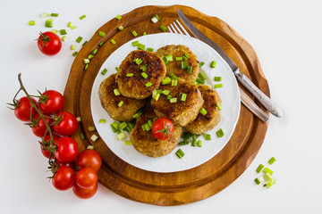 Roasted chicken cutlets with green onion on white plate and small cherry tomatoes on wooden background. Top view.