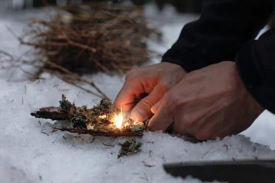 Man lighting a fire in a dark winter forest, preparing for an overnight sleep in nature, warming himself with DIY fire. Adventure, scouting, survival concept. .