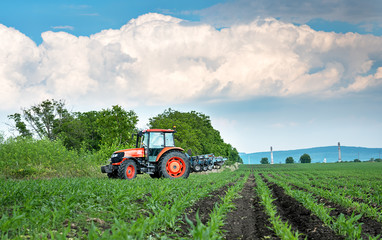 Obraz premium Close-up of agriculture red tractor cultivating field over blue