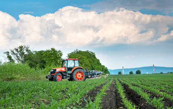 Close-up of agriculture red tractor cultivating field over blue