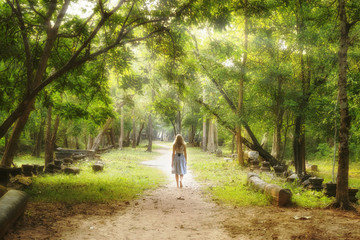 Young woman walking on path into an enchanted forest.
