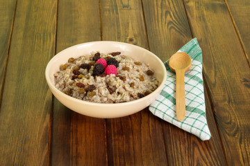Bowl oatmeal with raisins, spoon, cotton cloth on dark wood.