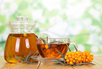 Jug, cup tea with sea-buckthorn berries on  green abstract.