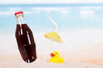 Bottle  cola, straw  and  rubber duck in  sand against  sea.