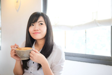 Asian woman drinking coffee and hold cup near window