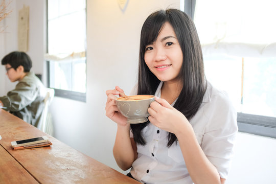 Asian woman drinking coffee and hold cup near window
