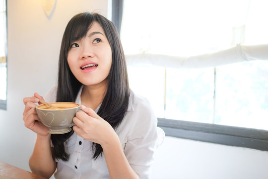 Asian woman drinking coffee and hold cup near window