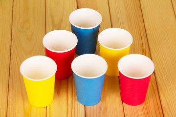 Multi-colored disposable paper cups on  background  light wood.