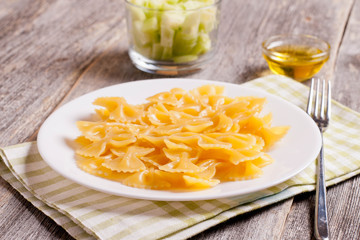 Farfalle on a white plate and olive oil on wooden background