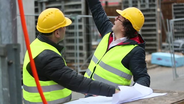 Engineers checking office blueprints pointing at something on a construction site