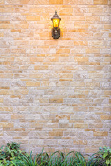 Exterior decoration of brick wall. The design consist of vintage hanging electrical lamp, natural brick block wall and small garden.