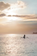 Indonesian fisherman in wide conical had goes with his catamaran into pink sunrise