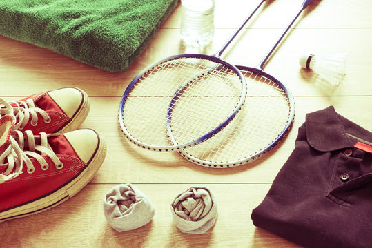 Rackets for badminton, shuttlecock, polo shirts, shoes, towel and water on a wooden floor. Retro effect,