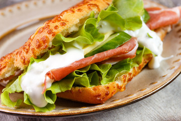Tasty ham Prosciutto sandwich with salad leaf, cheese and cucumber sauce in a cheese bread, homemade on breakfast.