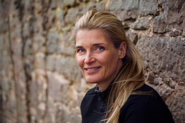 Portrait of smiling middle aged blond woman in front of stone wall