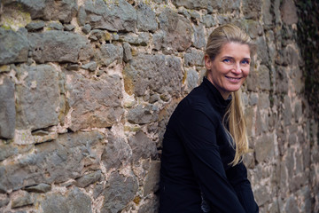 attractive middle aged blonde woman leaning against ancient wall in park after a run