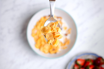 Corn flakes with milk on a spoon and berries pattern on a marble