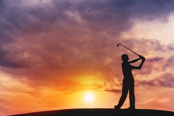 silhouette of boy golfer with golf club at sunset