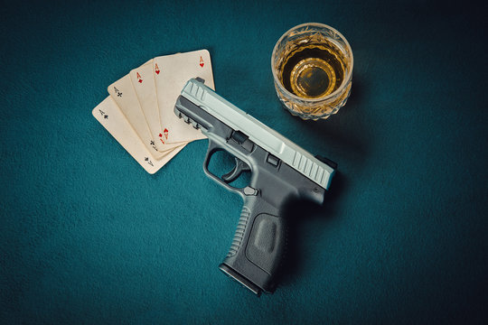 gun on four aces card and glass of scotch on poker table