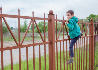 boy climbs up a high fence. concept escape from somewhere