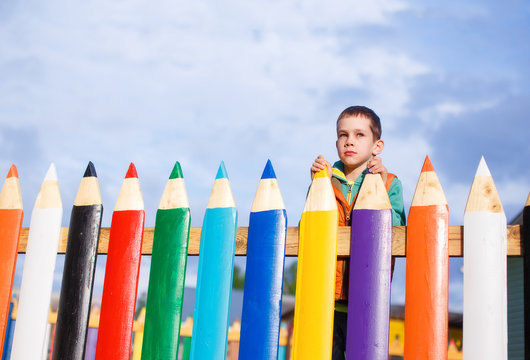 Boy Dreams Of Standing Behind The Fence Of Pencils. The Concept Of Accessible Education For Children. Copy Space For Your Text