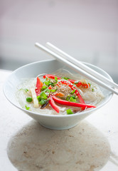 Asian rice noodles with vegetables and sesame in a bowl on a marble background, closeup