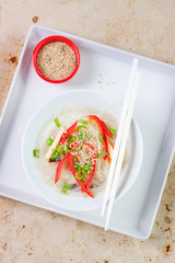 Asian rice noodles with vegetables and sesame in a bowl on a marble background, top view