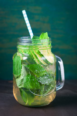 Tasty colourful drink with cold green tea, mint and cucumber in a glass jar on a vintage background, closeup