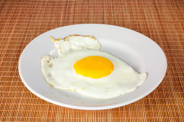 Fried egg in a white plate on a bamboo cover