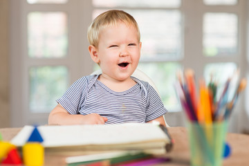 Blond boy laughing and crayons in front of him