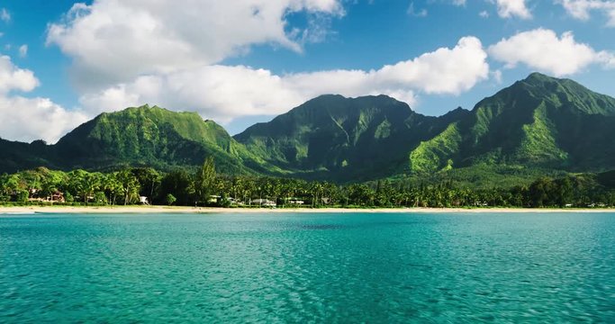 Aerial view flying over tropical blue ocean towards beautiful green mountains and white sandy beach on Kauai