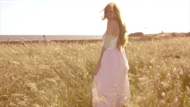 Beautiful woman with white dress walking in corn field in front of ocean at s