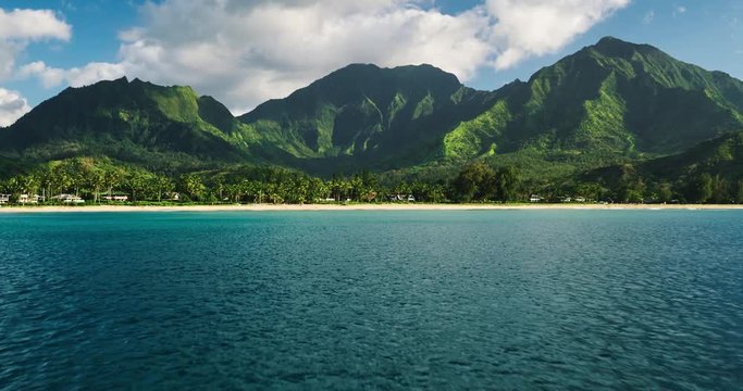Aerial view flying over tropical blue ocean towards beautiful green mountains and white sandy beach. Hanalei Bay, Kauai