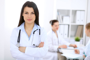 Fototapeta premium Brunette female doctor on the background of colleagues talking to each other in hospital