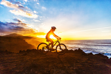 Fototapeta na wymiar Mountain biking MTB cyclist woman cycling on bike trail on coast at sunset. Person on bike by sea in sportswear with bicycle enjoying healthy active lifestyle in beautiful nature.