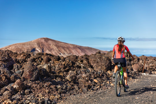Mountain biking woman MTB cyclist cycling on nature volcano volcanic trail on vacation travel against mountains. Tourist doing sports activity during summer holidays. Leisure tourism, ecotourism.